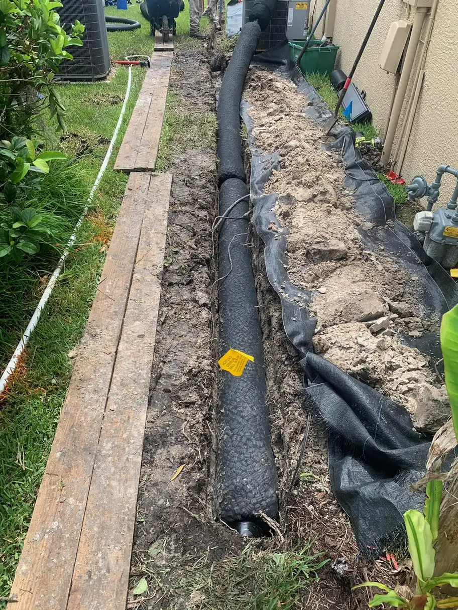 Corrugated drain pipe in a fabric-lined trench beside a board walkway