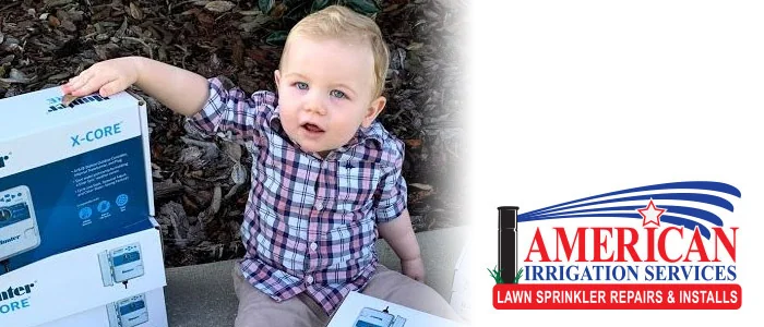Toddler sitting beside an irrigation controller box with the American Irrigation Services logo