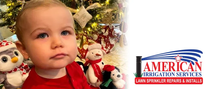 Toddler in front of a Christmas tree with holiday toys and the American Irrigation Services logo