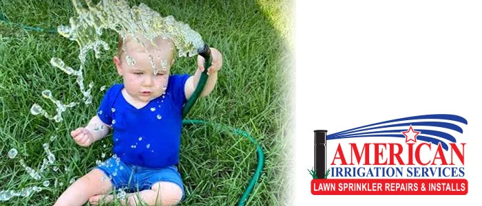 Toddler playing with a garden hose on the lawn with the American Irrigation Services logo